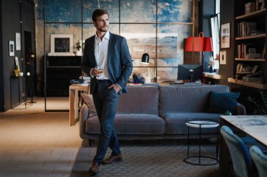 Genç yakışıklı işadamı dikilip kendi ofisinde bir bardak viski tutuyor..