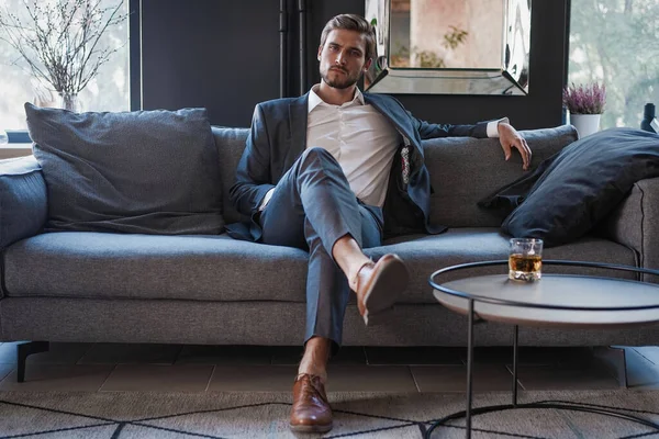 Молодий і чарівний бізнесмен думає про бізнес, сидячи на дивані в своєму сучасному офісі . — стокове фото