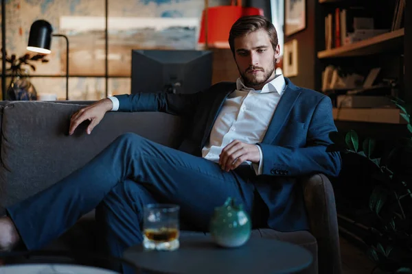 Jovem e charmoso empresário está pensando em negócios enquanto se senta no sofá em seu escritório moderno . — Fotografia de Stock