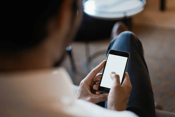 Sorrindo barbudo homem fazendo mensagem de texto no smartphone enquanto sentado sofá no escritório moderno. — Fotografia de Stock