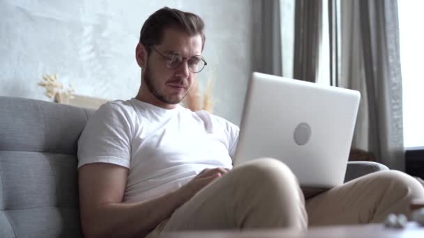 Hombre sentado en el sofá en casa, trabajando a distancia, disfruta de su trabajo, feliz de trabajar como freelancer — Vídeo de stock