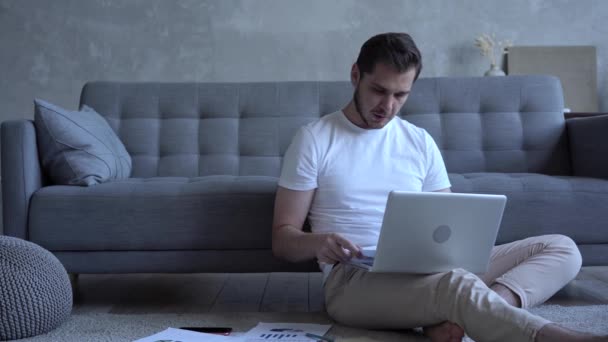 Focused man freelancer sitting on floor in cozy living room using computer — Stock Video