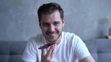 Genç sakallı adam koltukta oturuyor ve telefonla konuşurken gülümsüyor.