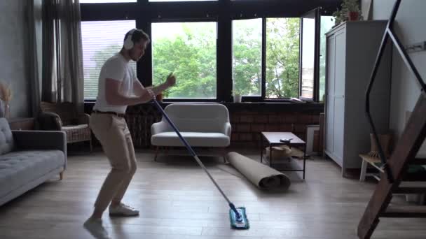 Radostný chlap v bezdrátových sluchátkách zpívá v mop mytí podlahy doma baví poslech rockové hudby — Stock video