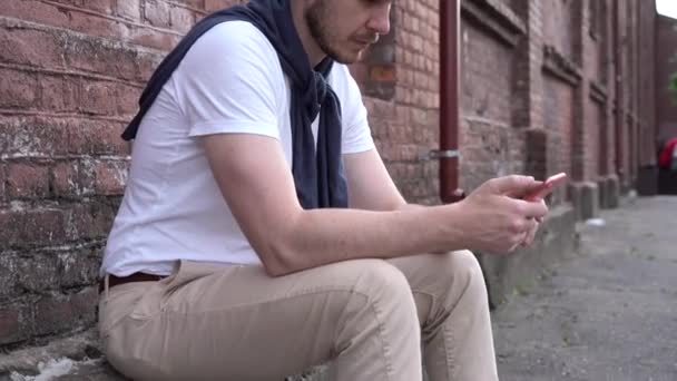 Sonriente chico leyendo el mensaje en el teléfono móvil al aire libre. Feliz hipster hombre mirando la pantalla del teléfono inteligente en el fondo urbano — Vídeos de Stock