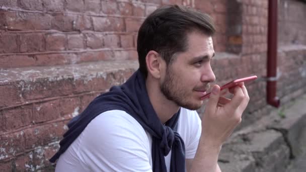 Un ragazzo sorridente che legge messaggi sul cellulare all'aperto. Felice hipster uomo cercando schermo dello smartphone in background urbano — Video Stock