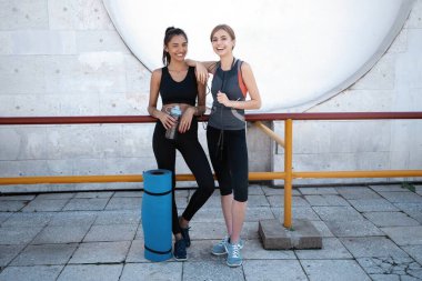 Spor antrenmanından sonra dışarıda yürüyen, konuşan ve birbirine sarılan iki mutlu, genç atletik kadın..