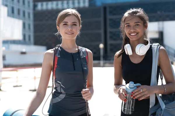 Dwie szczęśliwe uśmiechnięte młode wysportowane kobiety spacerujące razem na świeżym powietrzu po treningu sportowym, rozmawiające i przytulające się nawzajem. — Zdjęcie stockowe