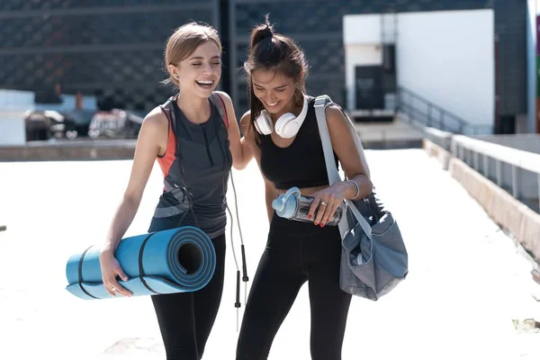 Dwie szczęśliwe uśmiechnięte młode wysportowane kobiety spacerujące razem na świeżym powietrzu po treningu sportowym, rozmawiające i przytulające się nawzajem. — Zdjęcie stockowe