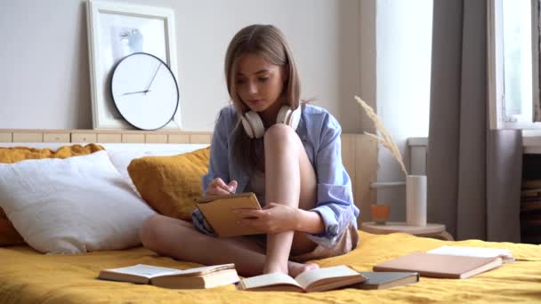 Feliz chica estudiante hermosa haciendo notas en cuaderno de papel, acostado en la cama — Vídeo de stock