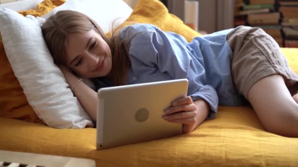 Junge Frau benutzt Gadget und spricht auf Tablet, das im Bett liegt — Stockvideo