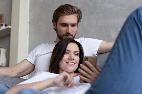 Happy couple enjoying media content in a smart phone sitting on a couch at home. — Stock Photo, Image