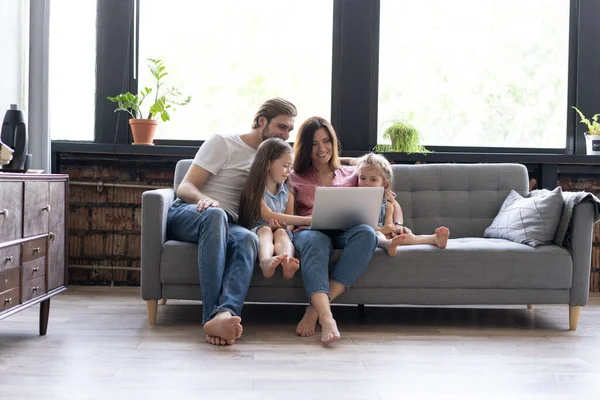 Des parents et des enfants souriants utilisant un ordinateur portable sur un canapé à la maison, profitant d'une vidéo drôle à l'ordinateur — Photo