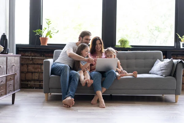 Des parents et des enfants souriants utilisant un ordinateur portable sur un canapé à la maison, profitant d'une vidéo drôle à l'ordinateur — Photo