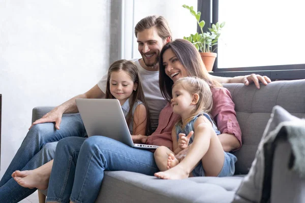 Des parents et des enfants souriants utilisant un ordinateur portable sur un canapé à la maison, profitant d'une vidéo drôle à l'ordinateur — Photo