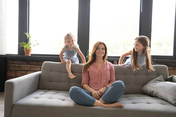 Femme calme se concentrant sur des exercices de yoga sur le canapé à la maison pendant que deux enfants bruyants rient, courent — Photo