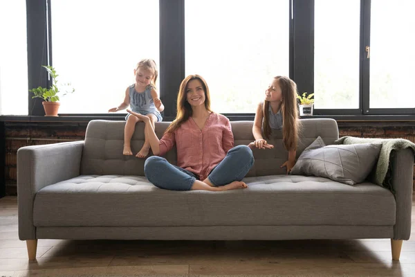 Calm woman concentrating on yoga exercises on couch at home while two noisy kids laughing, running — Stock Photo, Image
