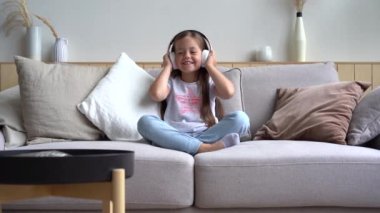 Kanepede otururken kulaklıkla müzik dinleyen tatlı küçük kız.