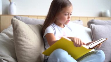 Esmer kız kanepede oturmuş kitap okuyor, sayfaları çeviriyor..