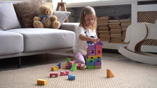 Menina bonito jaz no chão e brincando com blocos de construção coloridos — Vídeo de Stock