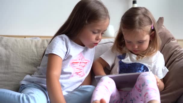 Hermanitas lindas sentadas una cerca de la otra, viendo algo en la tableta — Vídeos de Stock