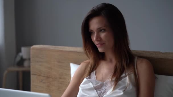 Jonge vrouw typen op laptop en zitten in bed in de ochtend — Stockvideo