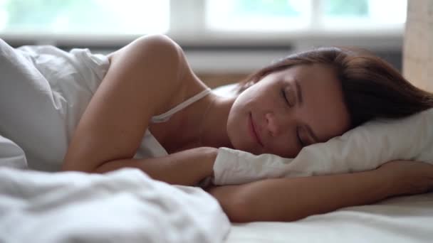 Mujer joven acostada y estirándose en la cama después de despertarse temprano en la mañana — Vídeo de stock