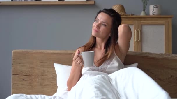 Hezká žena v pyžamu se usmívá a protahuje paže, zatímco sedí v posteli — Stock video