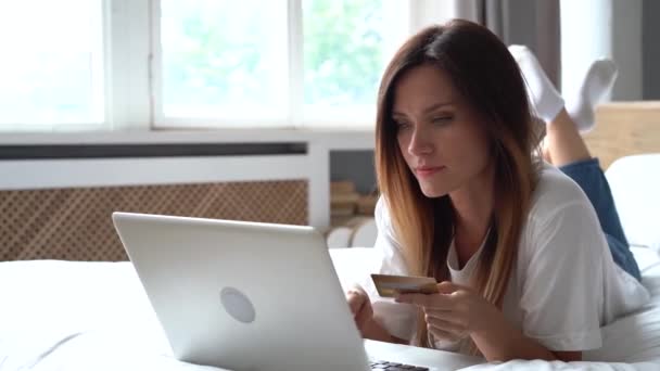 Vrouw doet online winkelen met laptop en creditcard terwijl ze op bed ligt — Stockvideo