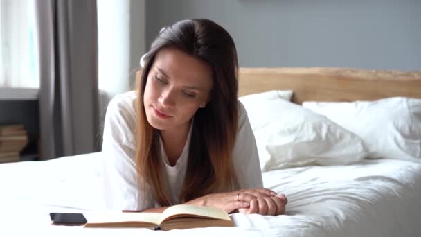 Tiempo libre en casa. Hermosa mujer acostada en la cama en casa y leyendo un libro — Vídeo de stock