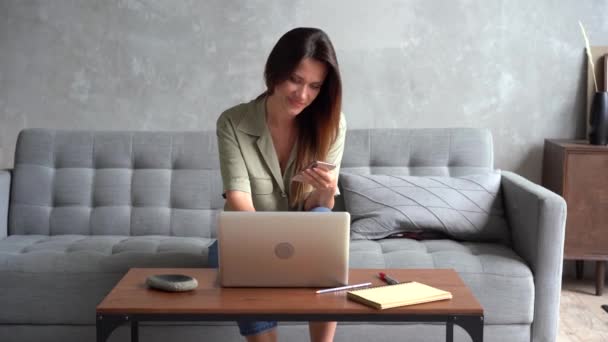 Joyeux jeune femme tenant smartphone bavarder dans les médias sociaux assis sur le canapé — Video