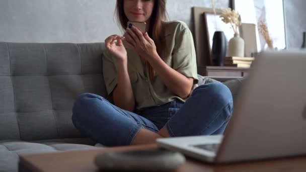 Szczęśliwa młoda kobieta trzyma smartfona na czacie w mediach społecznościowych siedzieć na kanapie — Wideo stockowe