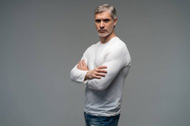 Gri arka planda, kot pantolon ve beyaz tişört giyen orta yaşlı neşeli bir adam..