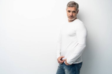 Beyaz arka planda, kot pantolon ve beyaz tişört giyen orta yaşlı neşeli bir adam..