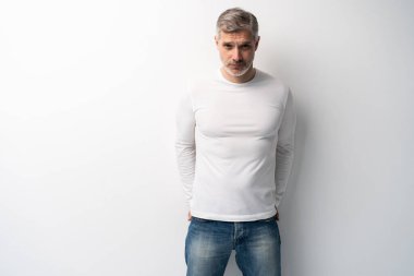 Beyaz arka planda, kot pantolon ve beyaz tişört giyen orta yaşlı neşeli bir adam..