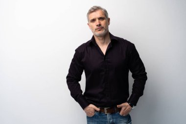 Beyaz arka planda, kot pantolon ve siyah gömlek giyen orta yaşlı neşeli bir adam..