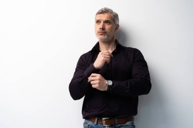 Beyaz arka planda, kot pantolon ve siyah gömlek giyen orta yaşlı neşeli bir adam..