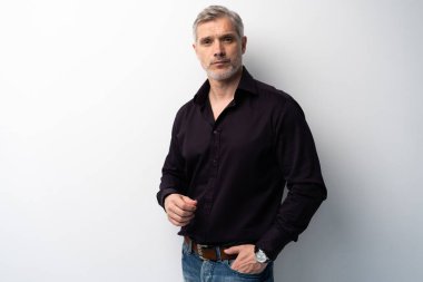 Beyaz arka planda, kot pantolon ve siyah gömlek giyen orta yaşlı neşeli bir adam..