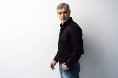 Beyaz arka planda, kot pantolon ve siyah gömlek giyen orta yaşlı neşeli bir adam..