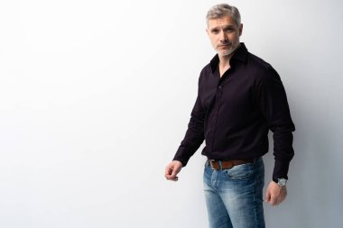 Beyaz arka planda, kot pantolon ve siyah gömlek giyen orta yaşlı neşeli bir adam..