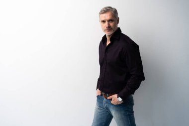 Beyaz arka planda, kot pantolon ve siyah gömlek giyen orta yaşlı neşeli bir adam..