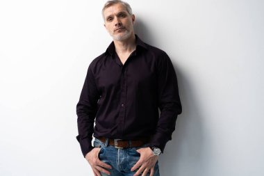Beyaz arka planda, kot pantolon ve siyah gömlek giyen orta yaşlı neşeli bir adam..