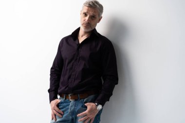 Beyaz arka planda, kot pantolon ve siyah gömlek giyen orta yaşlı neşeli bir adam..