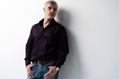 Beyaz arka planda, kot pantolon ve siyah gömlek giyen orta yaşlı neşeli bir adam..