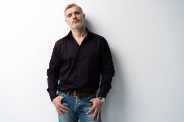 Beyaz arka planda, kot pantolon ve siyah gömlek giyen orta yaşlı neşeli bir adam..