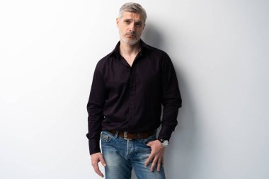 Beyaz arka planda, kot pantolon ve siyah gömlek giyen orta yaşlı neşeli bir adam..