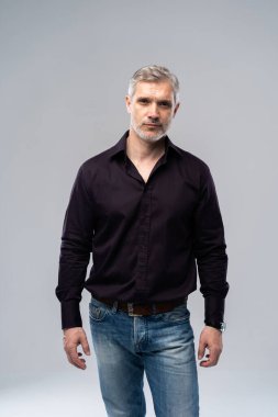 Beyaz arka planda, kot pantolon ve siyah gömlek giyen orta yaşlı neşeli bir adam..