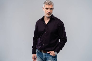 Beyaz arka planda, kot pantolon ve siyah gömlek giyen orta yaşlı neşeli bir adam..