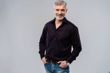 Beyaz arka planda, kot pantolon ve siyah gömlek giyen orta yaşlı neşeli bir adam..