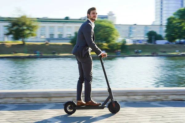 Joven hombre de negocios en un traje montando un scooter eléctrico en una reunión de negocios. —  Fotos de Stock
